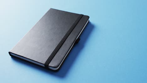 close up of closed black notebook with copy space on blue background in slow motion