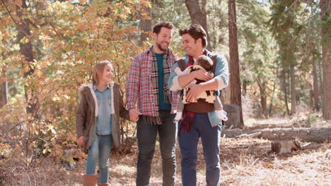 male parents in forest with baby and daughter walk to camera