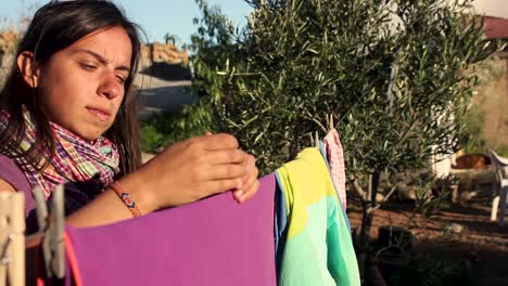 medium shot of a young girl hanging a purple towel with a clothespin to dry outside on a clothesline in the garden on a hot day