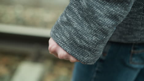 a close-up view of a man's hand wearing a grey suit jacket and blue jeans, walking along railway tracks, holding a fist and releasing his hand