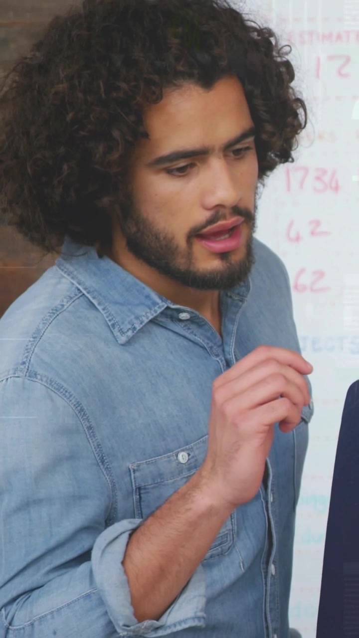Vertical video: Man noticing numbers on whiteboard, rolling sleeve, pointing and explaining finance