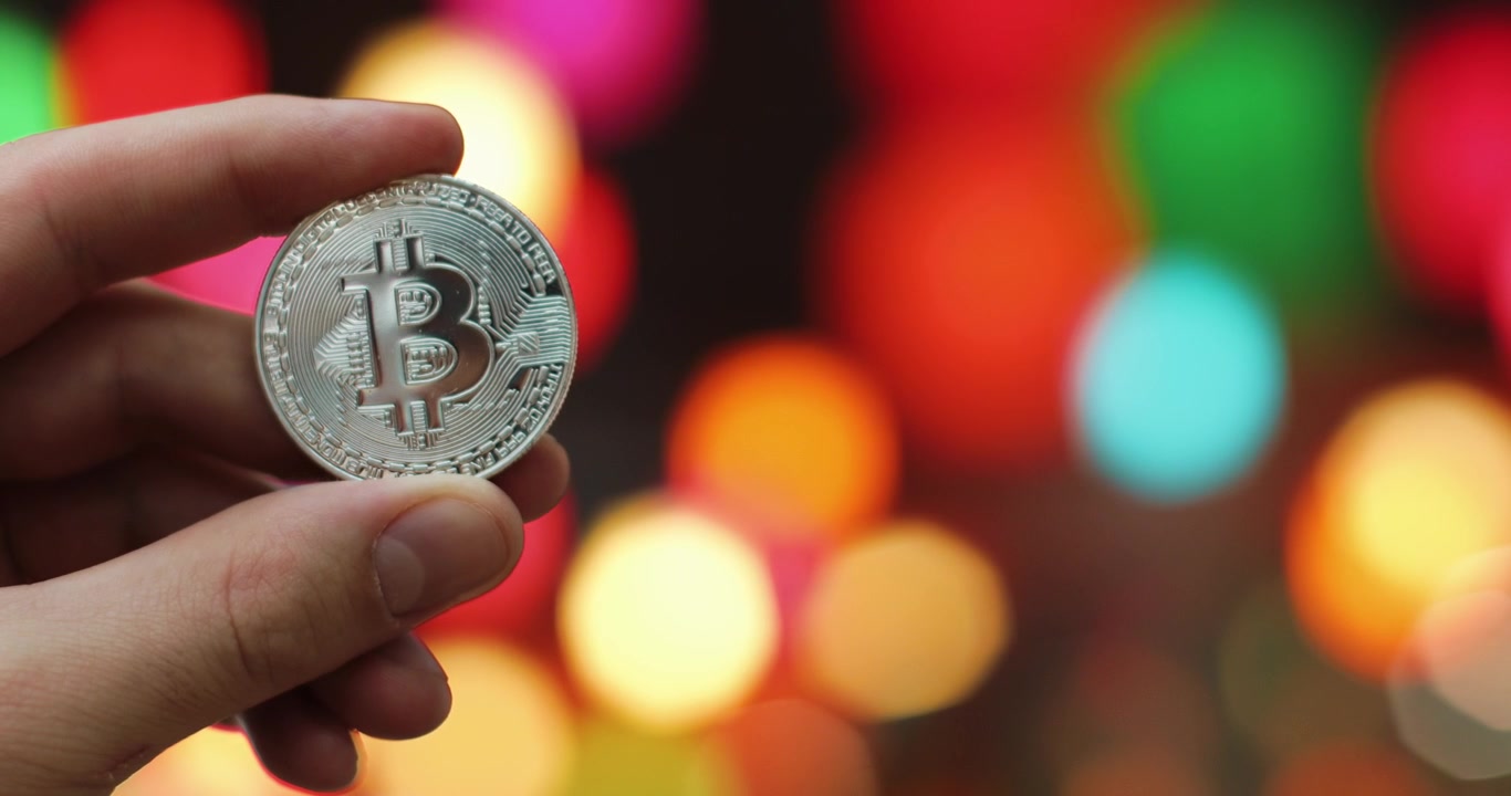 Mano che tiene una moneta Bitcoin con luci colorate sfocate