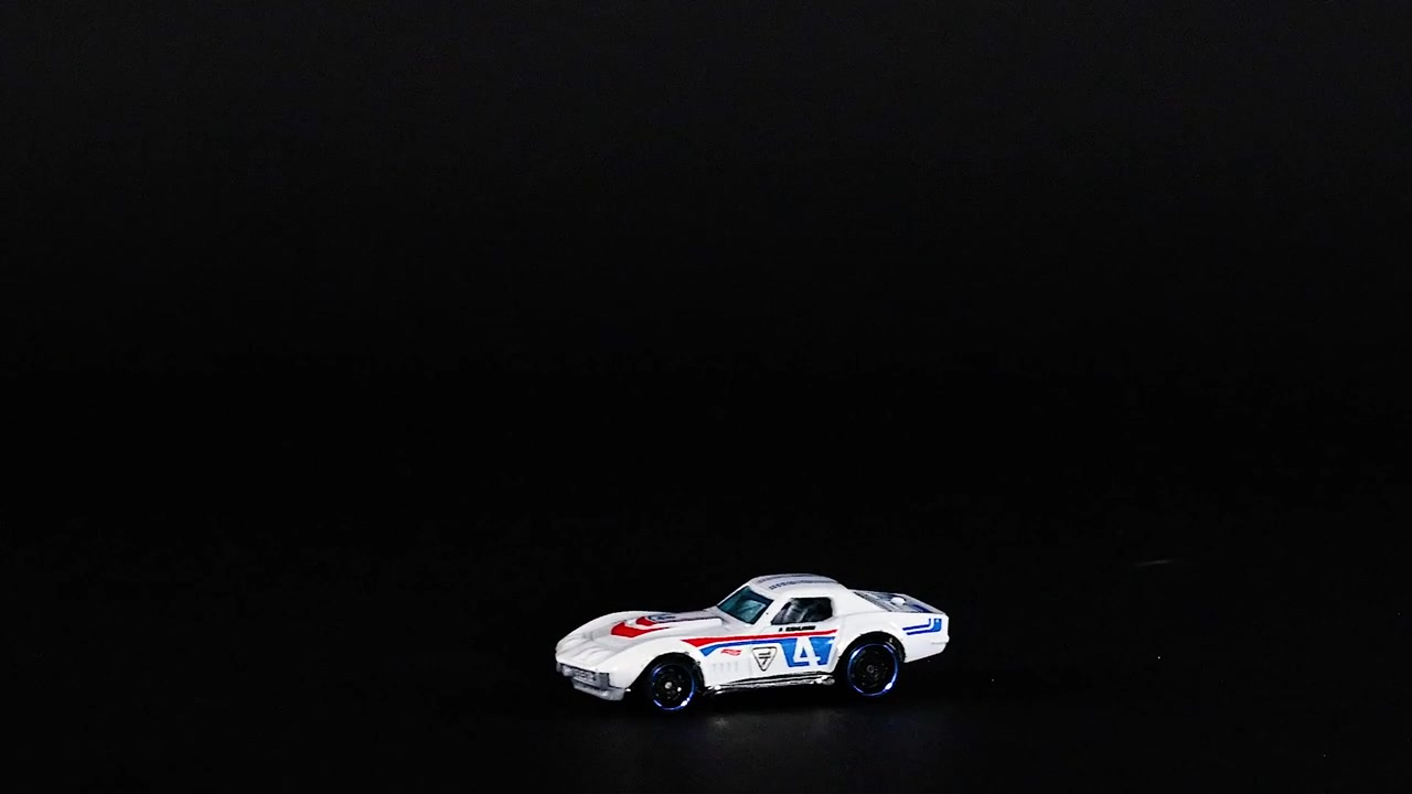 A yellow and a white toy car race across a dark surface, showcasing dynamic movement and contrast.