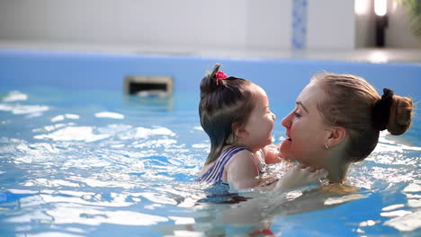 beautiful mother teaching cute baby girl how to swim in a swimming pool. child having fun in water with mom.