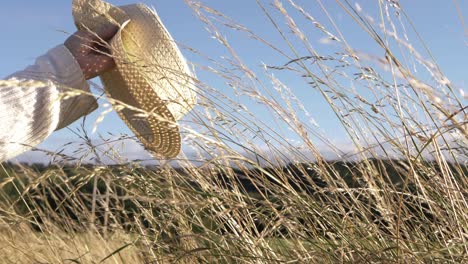 woman waving straw hat in tall grass medium shot