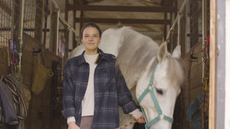 white horse eating hay while her owner is posing for the camera, holding it