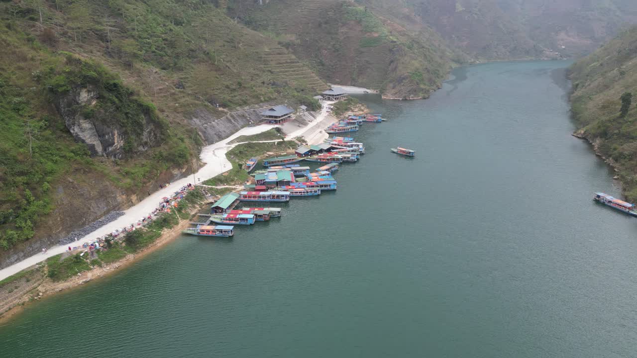 Vista aérea deslumbrante captura o tranquilo Rio Nho Quế e barcos coloridos atracados perto de paredes íngremes do cânion sob céus nublados, exibindo a beleza serena do Circuito Hà Giang no norte do Vietnã.