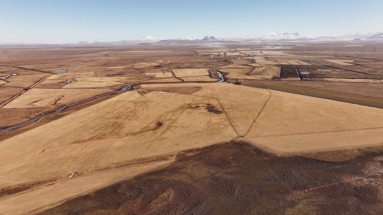 Aerial view of the yellow plains surrounding the Þjórsá (Thjorsa) River in Iceland. The golden hues of the farmland and open landscape stretch across the horizon under a clear winter sky.