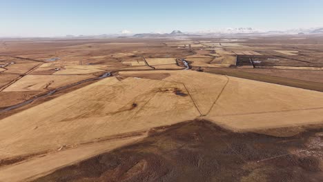 Aerial view of the yellow plains surrounding the Þjórsá (Thjorsa) River in Iceland. The golden hues of the farmland and open landscape stretch across the horizon under a clear winter sky.