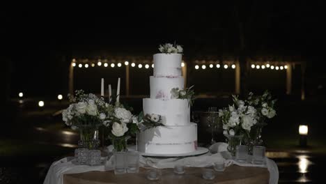 elegant white wedding cake surrounded by delicate floral arrangements at night