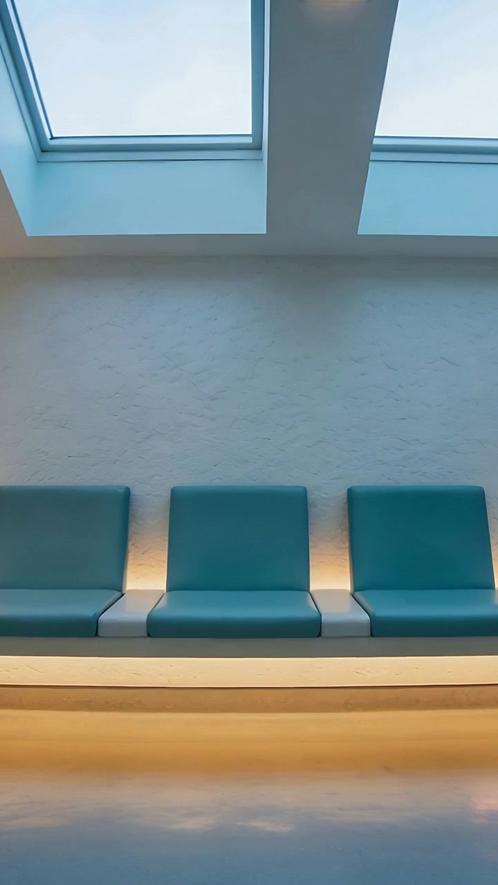 Vertical video: Tilting camera revealing three teal seats in lounge, showing skylights and warm LED