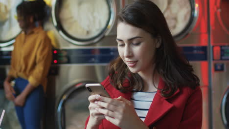 young pretty and stylish girl in yellow glasses standing in laundry service room and tapping on smartphone 2