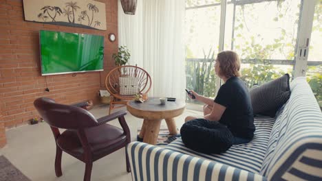 Mujer-Casual-Encendiendo-El-Televisor-En-La-Pantalla-De-Croma-Y-Sentándose-En-El-Sofá-De-Casa