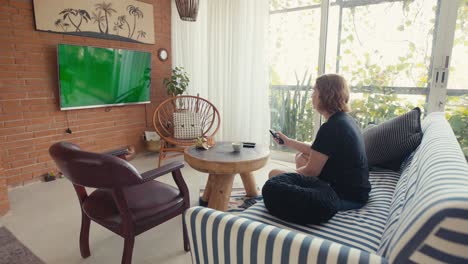 mujer casual encendiendo la tv en la pantalla clave de chroma y sentarse en el sofá en casa