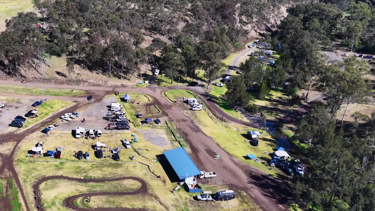 Drone captures motocross track, vehicles, and people at outdoor event under clear daylight