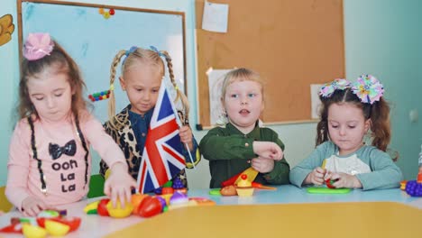 positive kids with flags at during the lesson. little children playing with fruit patterns and waving flags. british and german flags in girls hands.