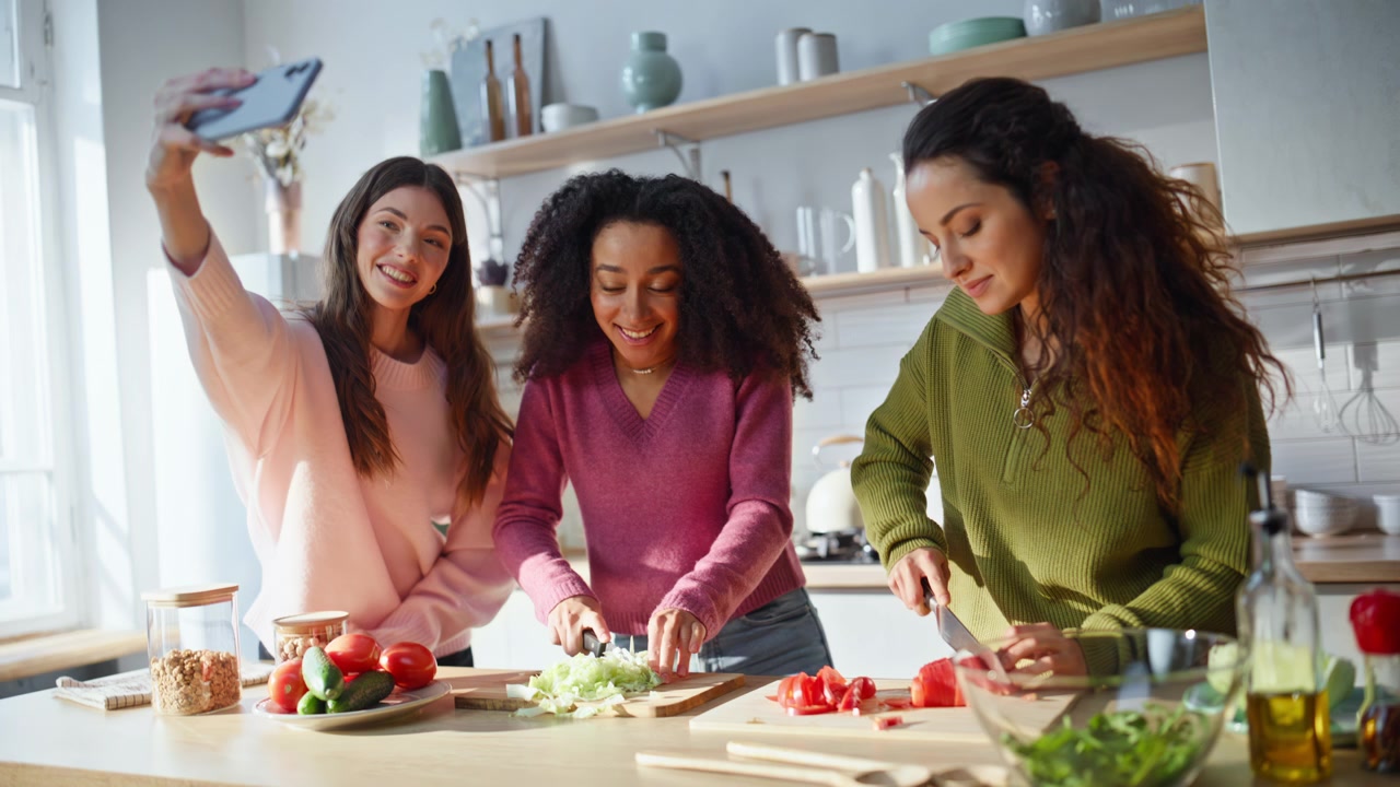 Happy women cooking kitchen together posing cellphone photo. Smiling friends