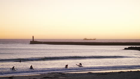 Vista-Estática-Del-Grupo-Con-Kayaks-Superando-Las-Olas-Al-Atardecer,-Rompeolas-Y-Telón-De-Fondo-Del-Barco-De-Carga