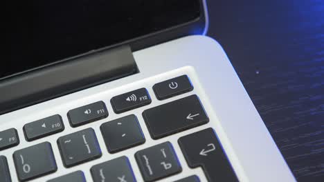 Hand is pressing power on key on laptop computer, close up. Finger presses power button to turn on laptop. Man is pushing laptop power button
