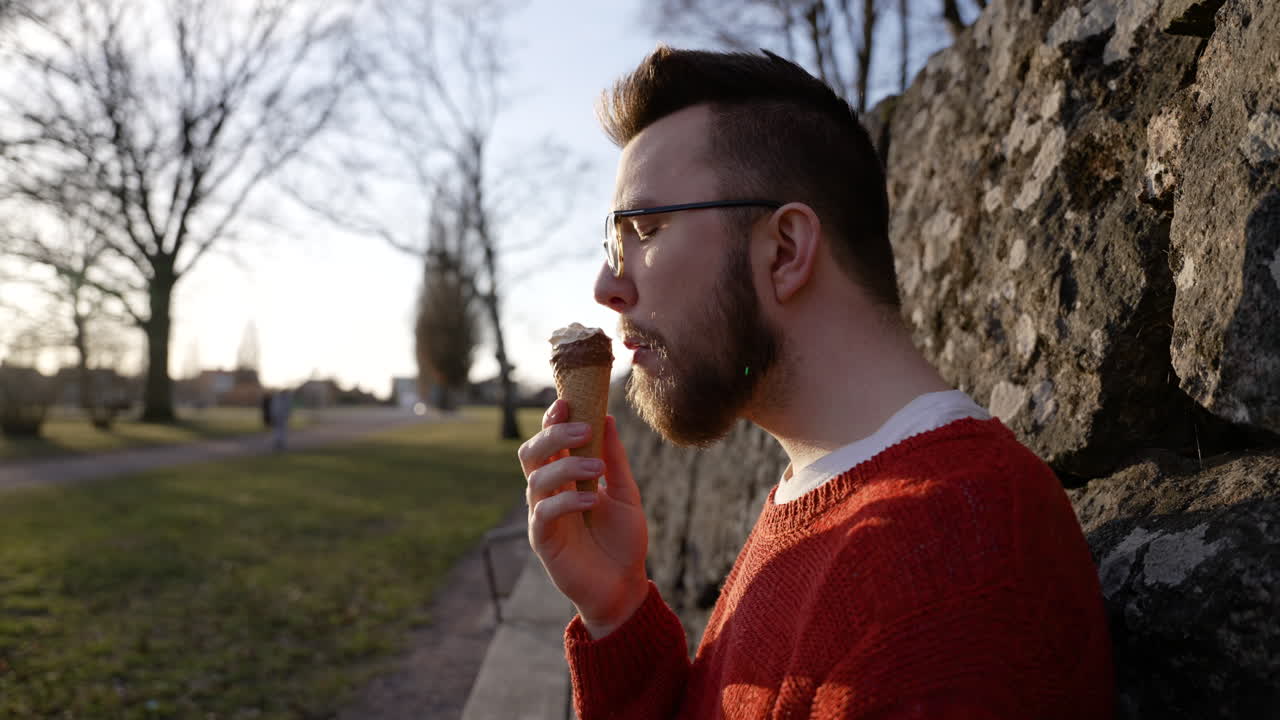 comiendo cucurucho de helado caucásico europeo hombre sentado en un banco degustación frío congelado delicioso postre azúcar dulce vainilla chocolate fudge verano disfrutar sol caliente calentar tiempo morder feliz satisfecho sueco