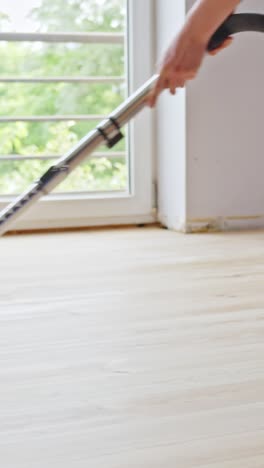vertical scene showing a vacuum cleaner being used to clean a newly sanded wooden floor in a sunlit room during a home renovation, preparing the surface for further treatment or coating