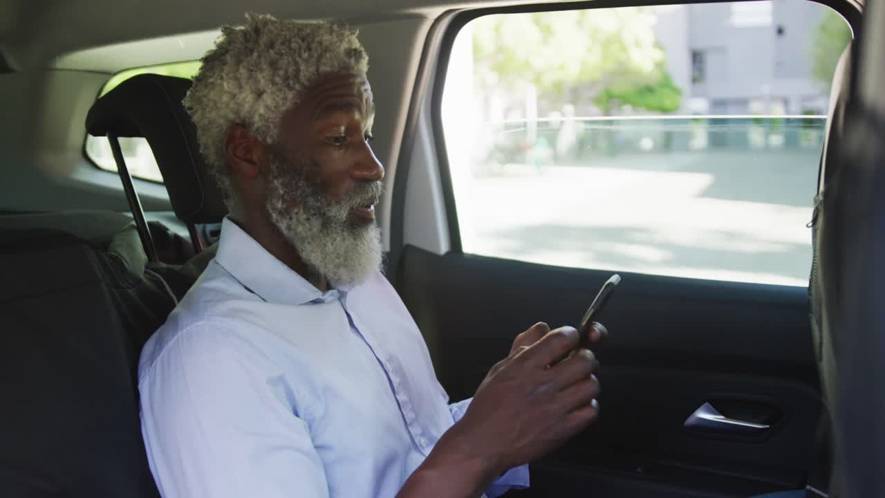 hombre mayor afroamericano que usa un teléfono inteligente mientras está sentado en el coche