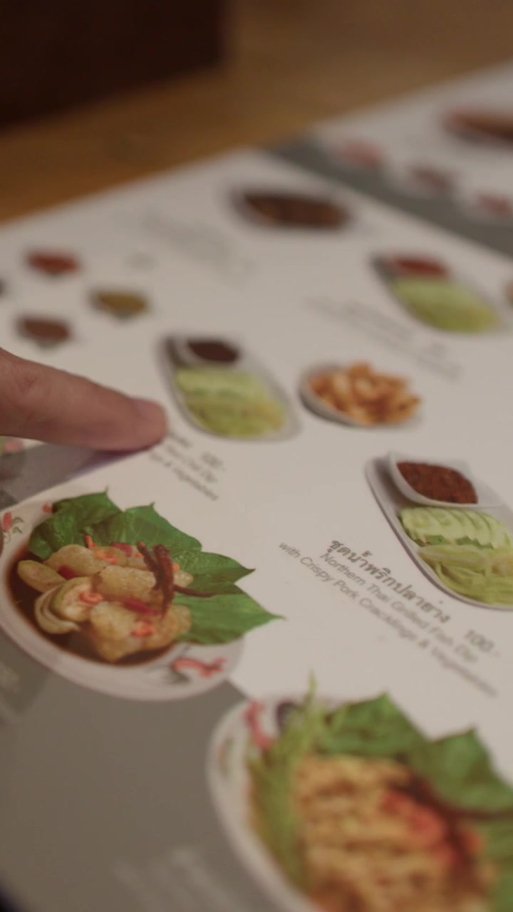 Nærbillede af hænder, der peger på madbilleder på en menu i varm indendørs belysning.