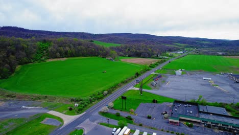 Drone-shot-of-a-tractor-applying-chemicals-on-a-green-field-next-to-a-highway,-depicting-farm-management