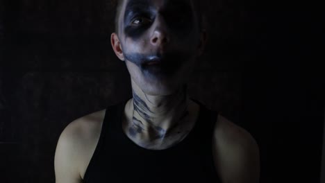 young man with a scary dark clown makeup appearance talking alone front of black background halloween carnival evil fear