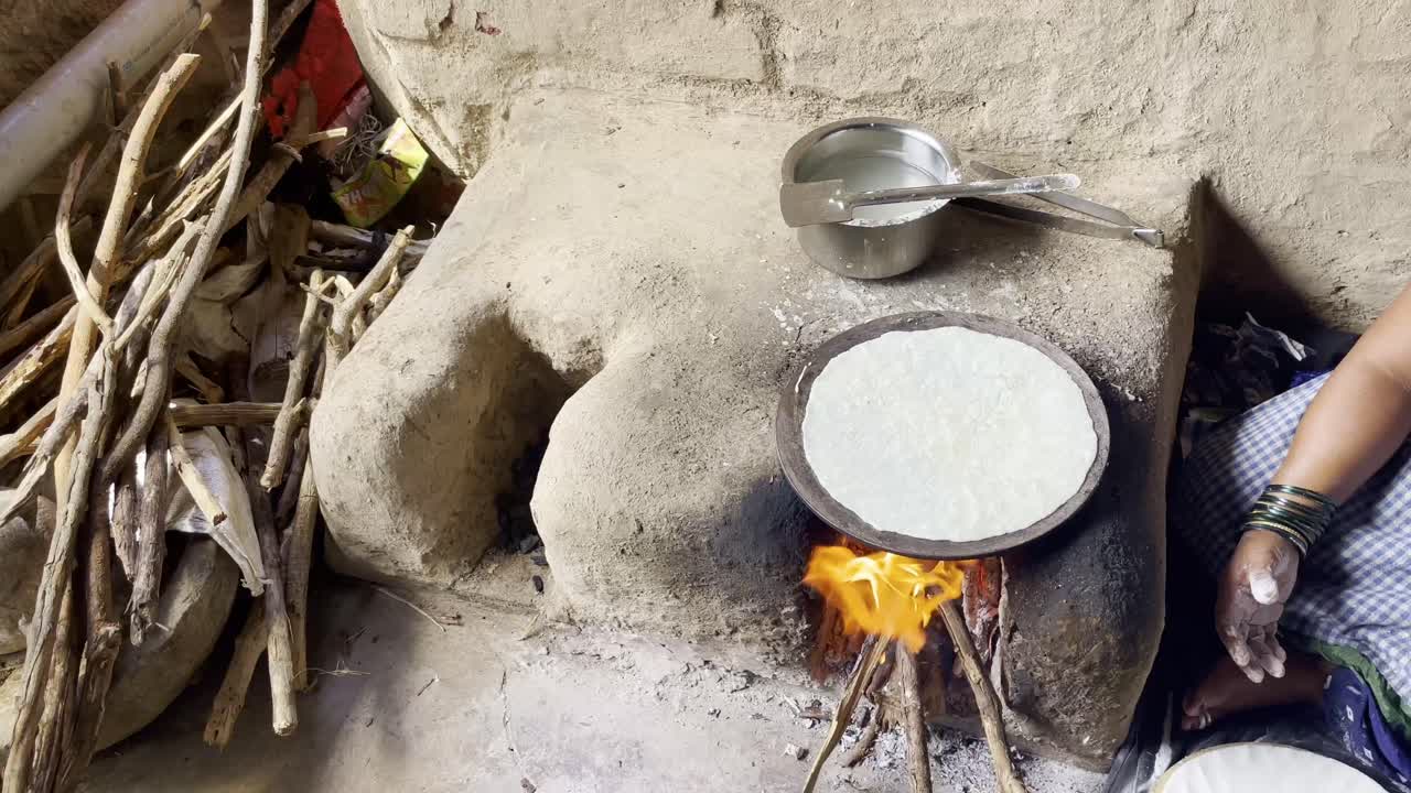 Indisk kvinna bakar traditionellt indiskt bröd, bhakri, med ved i lerugnar (chulhas) i Maharashtra, Indien, 4K.