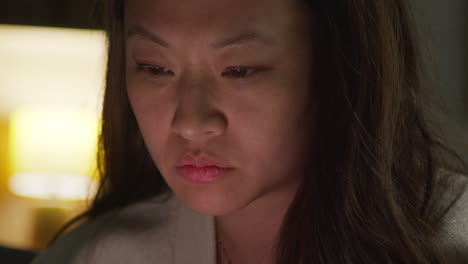 close up of stressed anxious woman spending evening at home sitting on sofa reacting to internet or social media news message or story on mobile phone