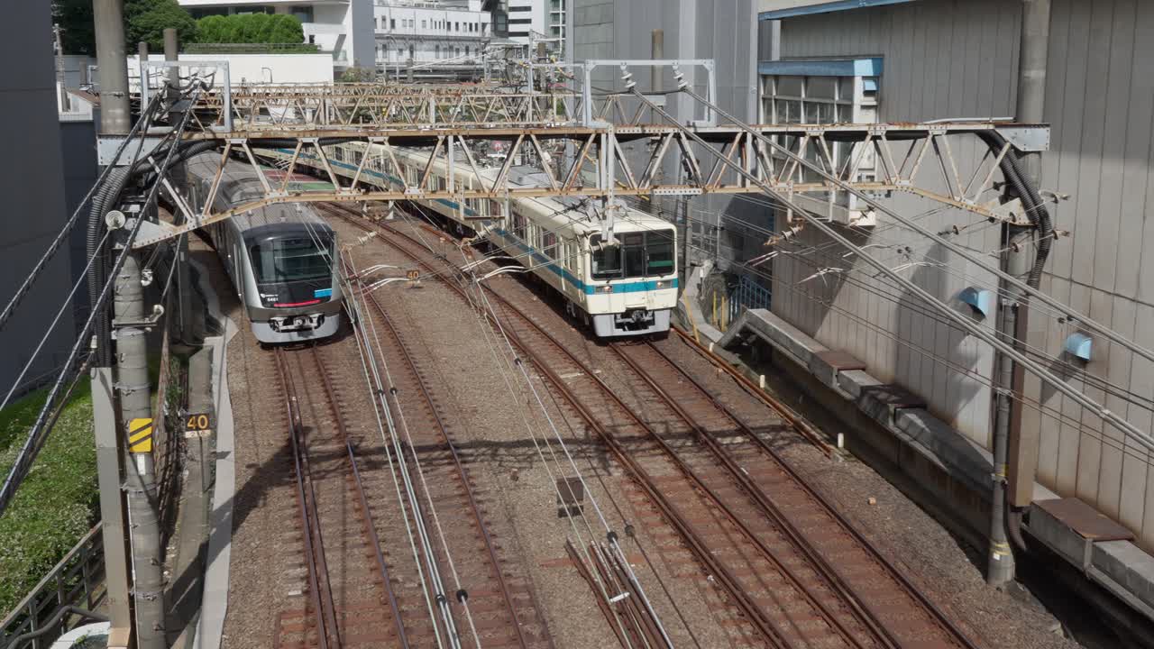 An overhead shot of two different commuter trains traveling on parallel, elevated tracks in an urban area of Tokyo