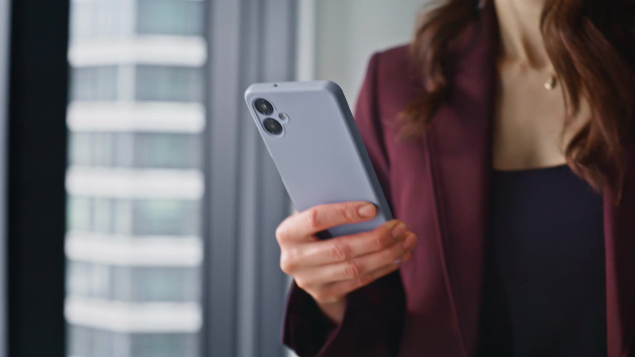 Primo piano della mano di una donna che usa lo smartphone mentre passeggia nel corridoio dell'ufficio. Donna sconosciuta che cammina.