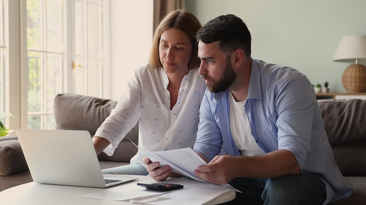 una pareja se sienta en una mesa con una computadora portátil revisando facturas, comprobando gastos