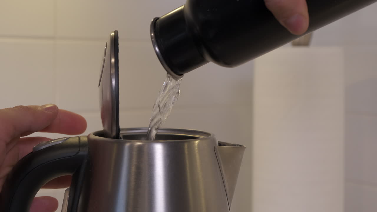 Jeune homme versant de l'eau d'une bouteille d'eau noire dans une bouilloire à faire bouillir