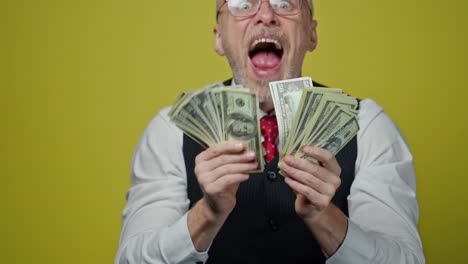 excited mature man waving dollars. happy funny elderly businessman showing banknotes on camera with opened mouth. positive emotions.