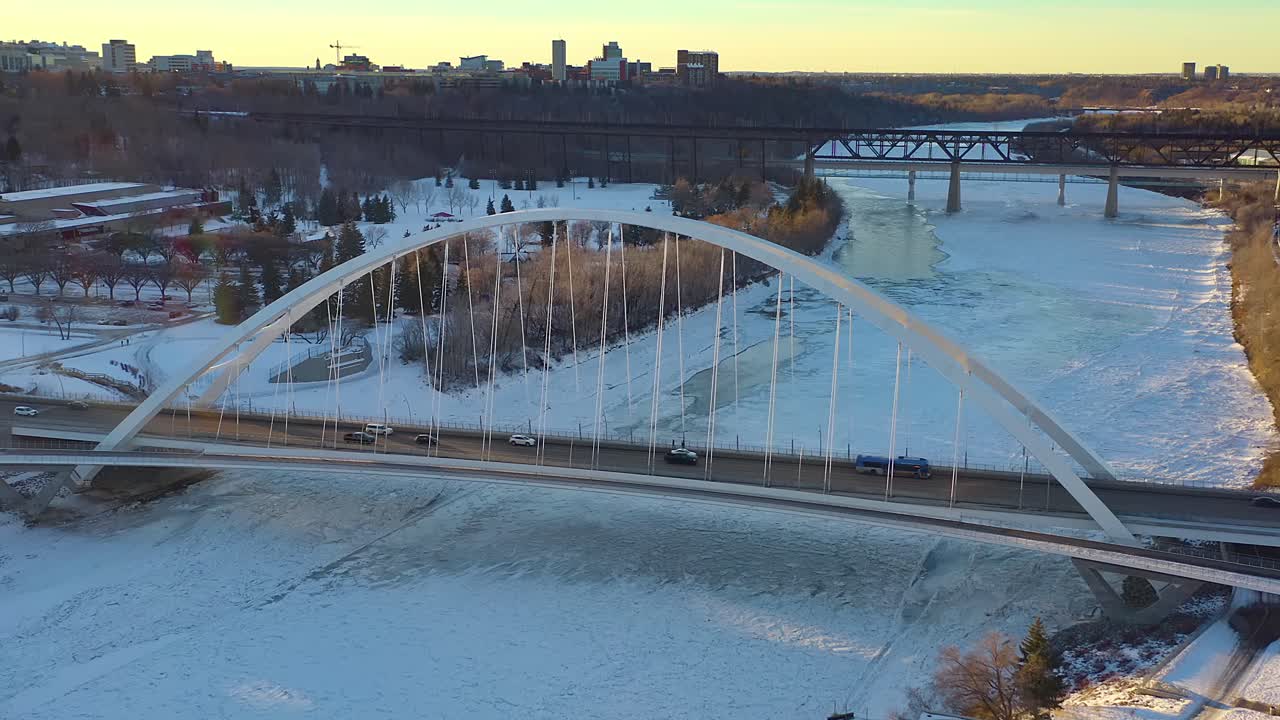mosca aérea soleada sobre el puente moderno walter dale blanco sobre el río saskatchewan norte cubierto de hielo con el cruce vintage de bajo nivel adelante rodeado de parientes y el parque victoria en edmonton ca 1-4