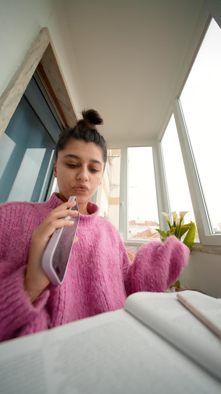 Giovane donna che parla al telefono mentre studia con un libro