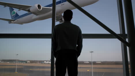 man in silhouette looking at airplane through airport window