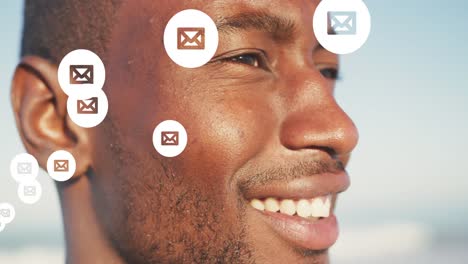 Animation-of-social-media-email-icons-over-close-up-of-smiling-man-on-beach