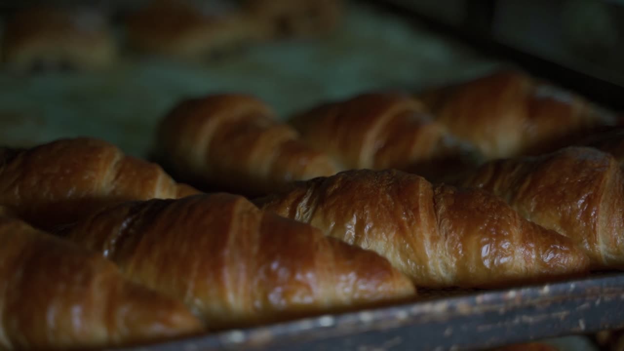 un panadero retira varios croissants regulares y de chocolate de una bandeja de horneado en una panadería