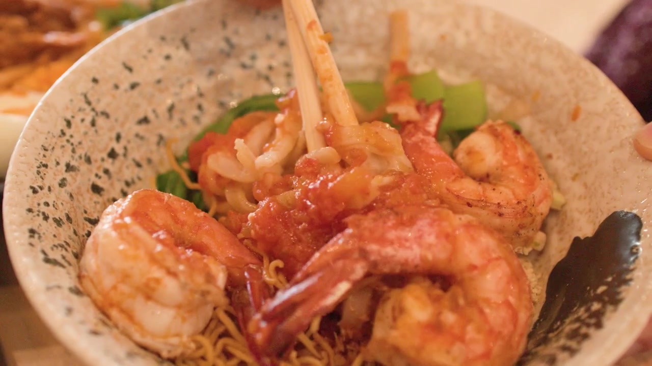 Primo piano di bacchette che sollevano noodles Shan da una ciotola con gamberi a Bangkok, Thailandia.