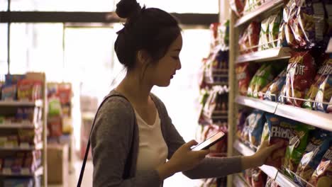 A Young Woman Engages with Her Phone While Shopping for Snacks in a Supermarket Aisle Filled with Colorful Potato Chip Bags