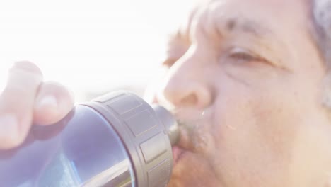 video en primer plano de un hombre biracial mayor bebiendo de una botella de agua en el sol.