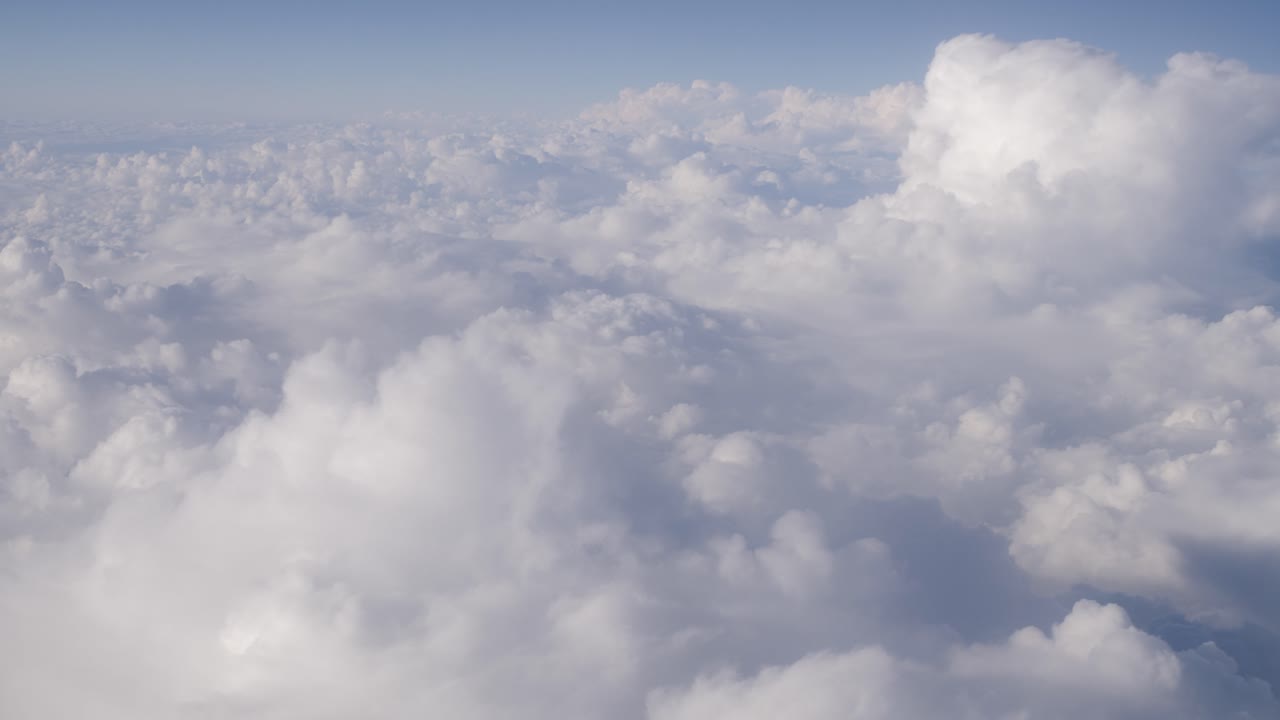 Breathtaking aerial view of fluffy clouds stretching across sky, taken from an airplane. The soft white clouds fill the scene, with blue sky in the background creating serene and peaceful atmosphere