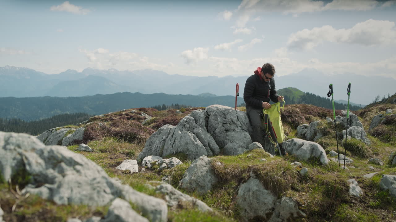 un excursionista sentado en la roca en la cima de una montaña y tomando un sorbo de su termo