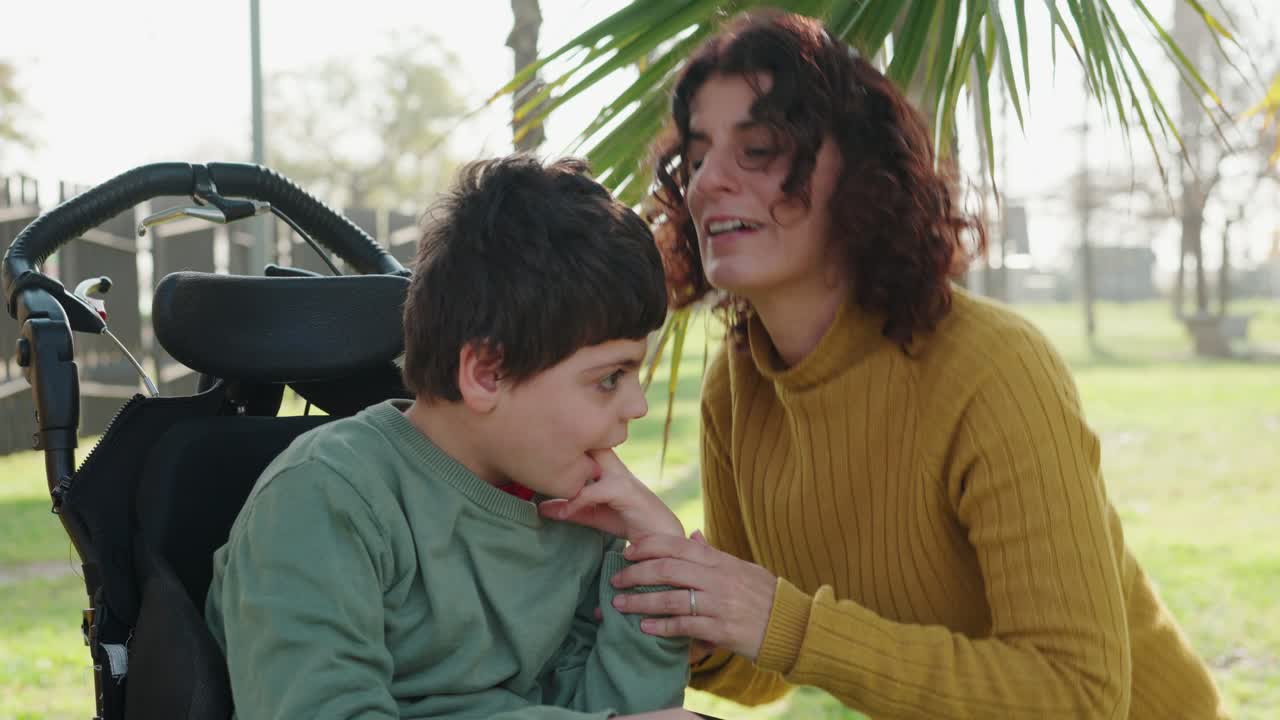 A mother and child in a wheelchair share a tender moment in the park