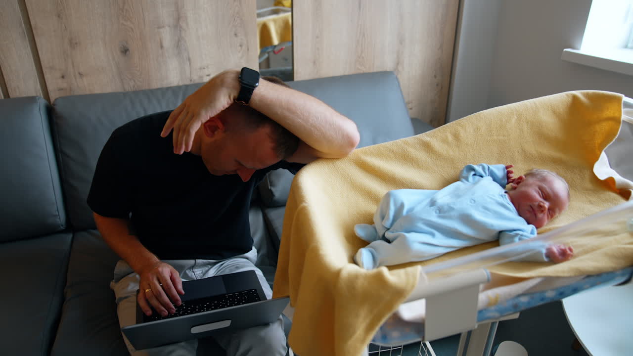 Tired dad combining work and taking care of the child. Man falls asleep over his laptop.