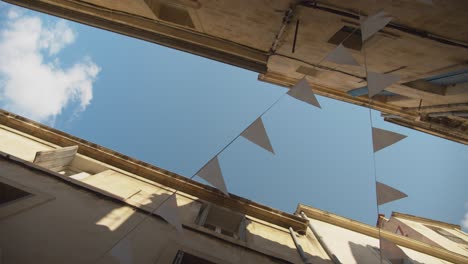 Vista-De-La-Calle-De-Ensueño-En-ángulo-Bajo-De-Montpellier,-Francia,-Mirando-Hacia-Las-Cuerdas-De-Banderines-Y-Cielos-Azules-Con-Nubes-Blancas-Esponjosas