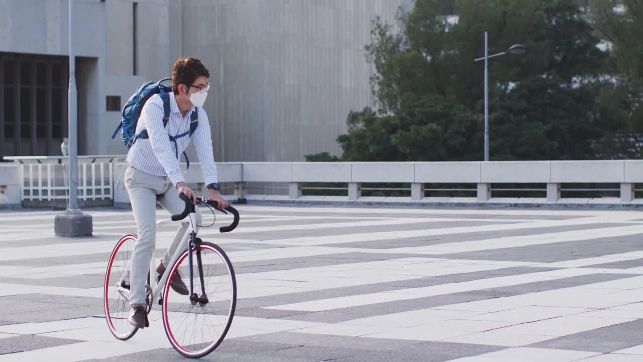 아시아 남자가 회사 공원의 지붕에 자전거를 타고 얼굴 마스크를 쓰고 있습니다.